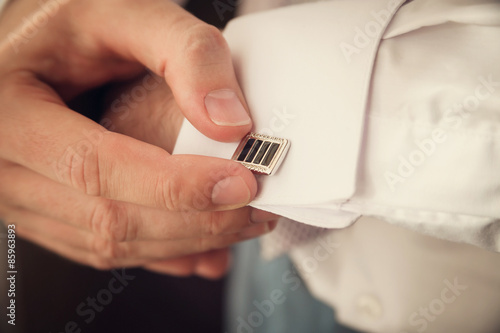 groom putting on cuff-links as he gets dressed in formal wear close up