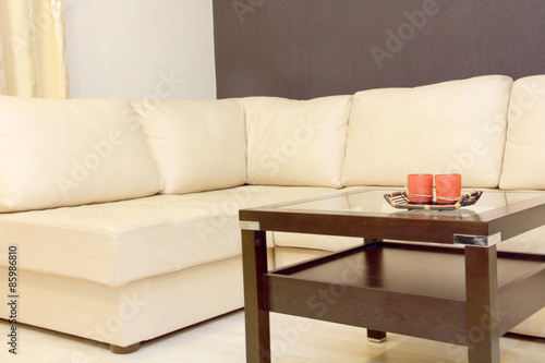 Interior with coffee table and white corner leather sofa .