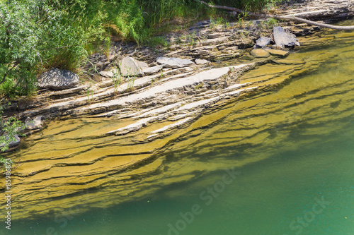 Fototapeta Naklejka Na Ścianę i Meble -  Bank of emerald mountain river consisting of layers of rock.
