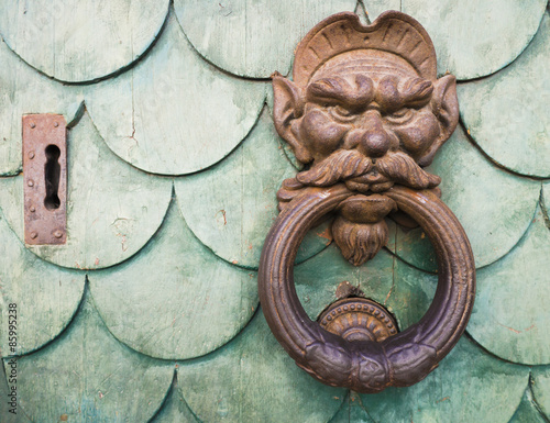 Iron goblin face doorknocker on green wooden door 