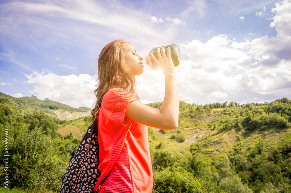 thirsty girl drinking from water bottle while ago tracking in the mountains - people, drink and nature concept