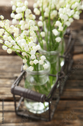 Lily of the Valley in bottles on brown wooden background