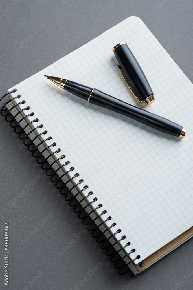 A spiral notebook with black ball pen over the grey background A spiral notebook with black ball pen over the grey background