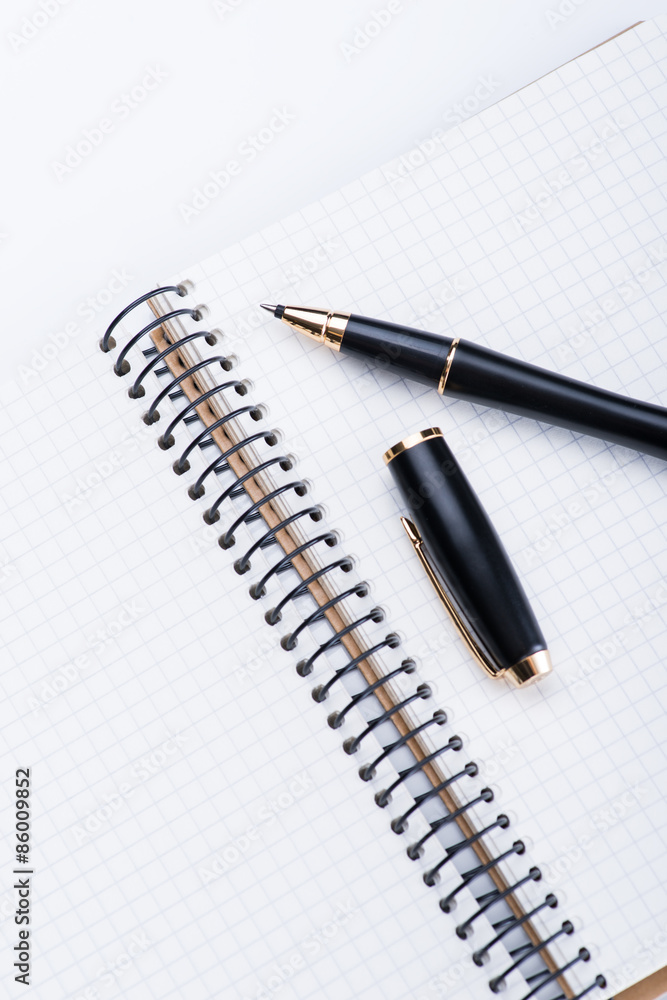 A spiral notebook with black ball pen over the white background, isolated A spiral notebook with black ball pen over the white background, isolated