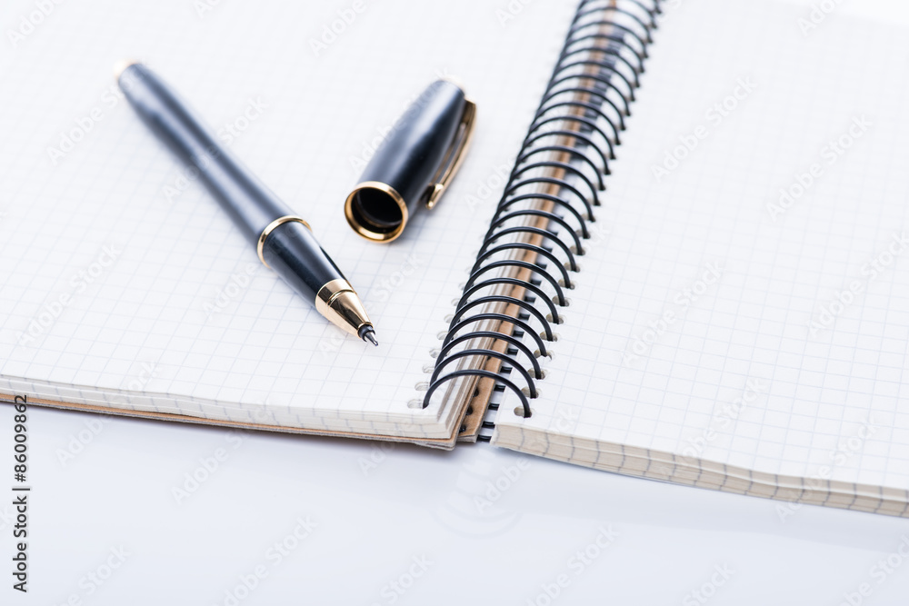 A spiral notebook with black ball pen over the white background, isolated A spiral notebook with black ball pen over the white background, isolated