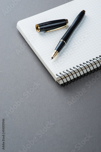 A spiral notebook with black ball pen over the grey background