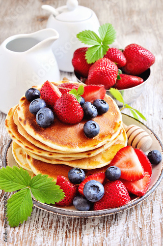 Pancakes with fresh strawberries, blueberries, maple syrup and honey, selective focus