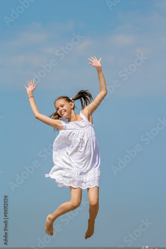 Girl in a white sundress jumps over the sea