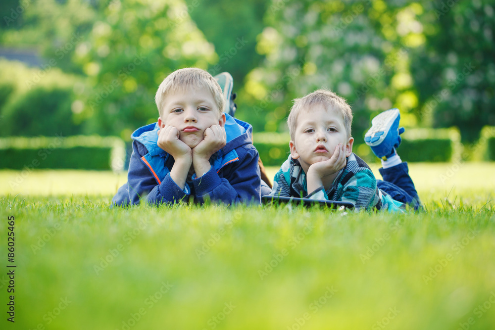 Siblings using a tablet, yingon grass in the park in suny day Siblings using a tablet, yingon grass in the park in suny day
