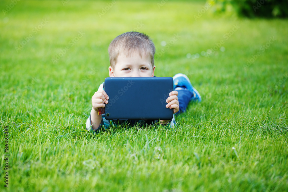 Cute boy lying on grass in park and using tablet pc Cute boy lying on grass in park and using tablet pc