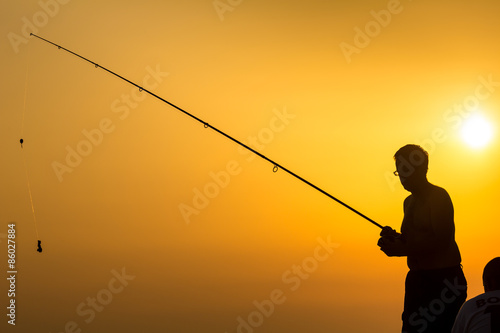 Fisherman's silhouette on the beach at colorful sunset