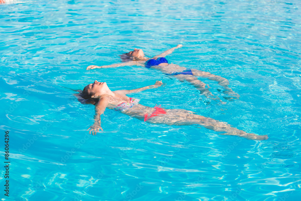 Two beautiful women lying on swimming pool water surface