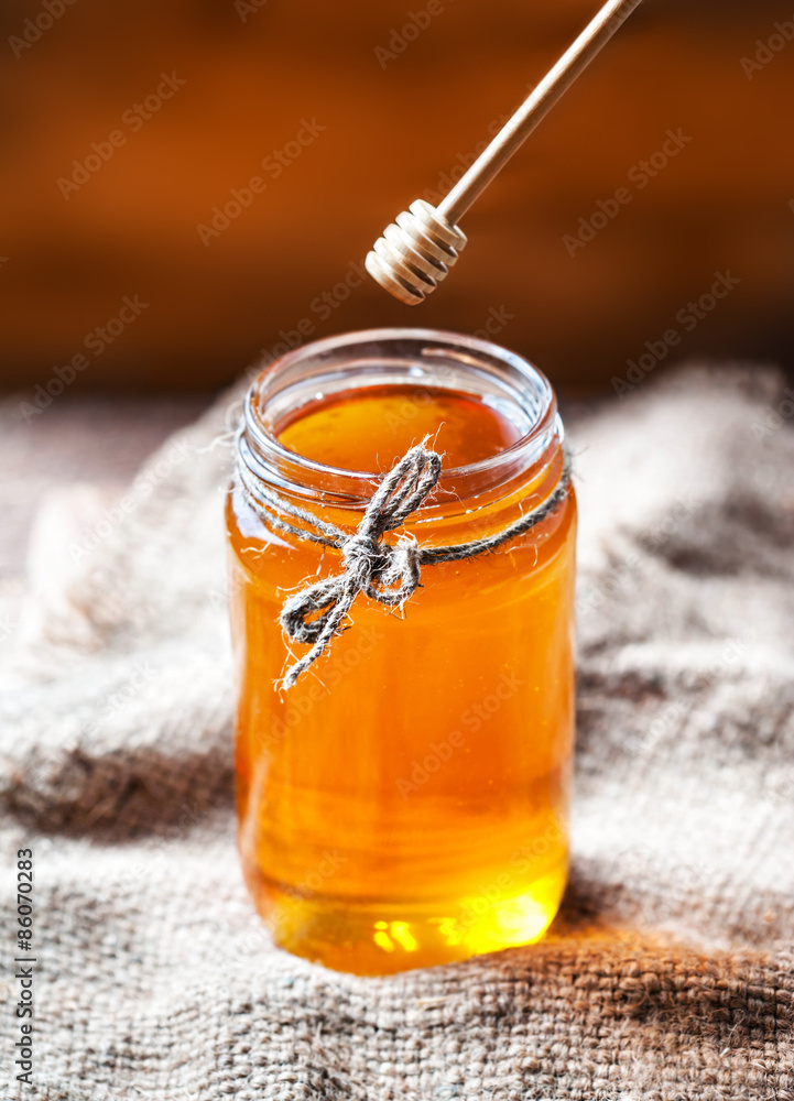 Honey in a glass jar with honey dipper on vintage wooden backgro Honey in a glass jar with honey dipper on vintage wooden backgro
