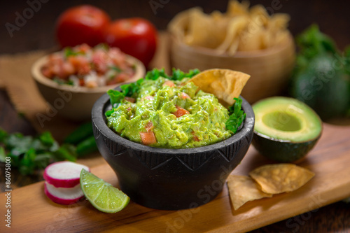 Mexican restaurant style side of Guacamole food and chips on a wood cutting board vertical shot with salsa