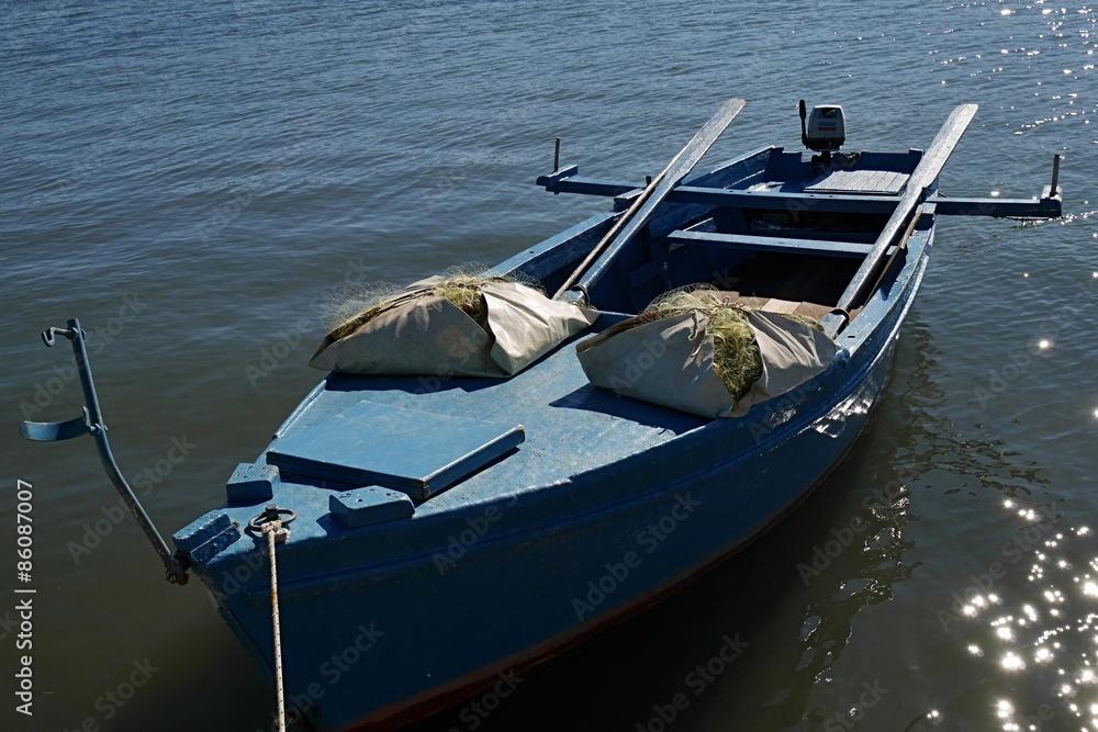 Blue fishing boat with oars, packed fishnets and motor engine