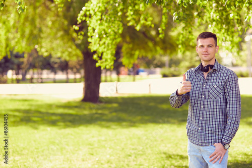 Smiling young man in a shirt with earphones shows a thumb in par