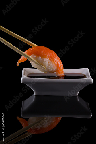 Salmon sushi nigiri in chopsticks with soy sauce over black background