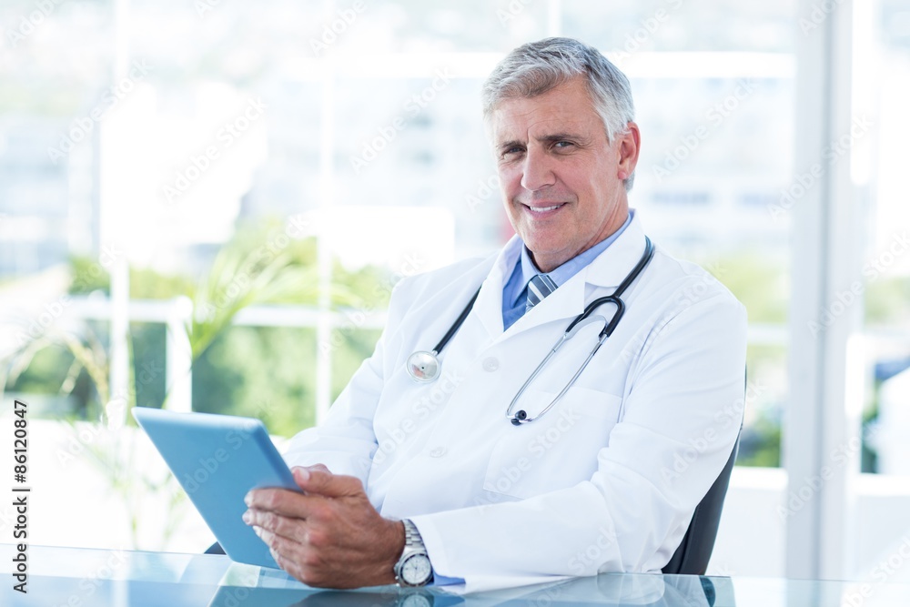 Smiling doctor sitting at his desk and holding tablet Smiling doctor sitting at his desk and holding tablet