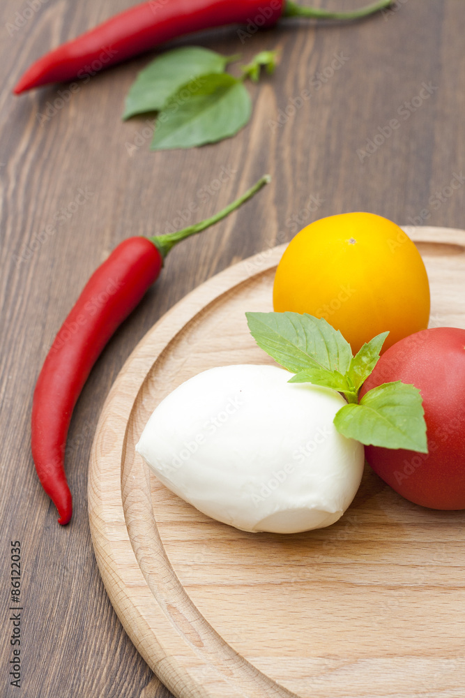 Mozzarella with herbs, fresh vegetables, chilli, on a wooden round board, selective focus Mozzarella with herbs, fresh vegetables, chilli, on a wooden round board, selective focus