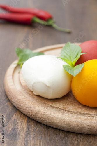 Mozzarella with herbs, fresh vegetables, chilli on a wooden round board, selective focus