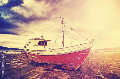 Vintage toned picture of an old stranded boat on a beach at sunset.
