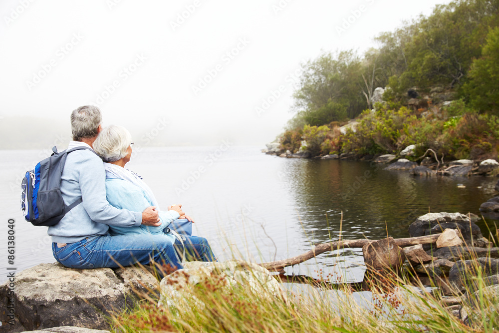 Senior couple sitting together by a lake admiring the view Senior couple sitting together by a lake admiring the view