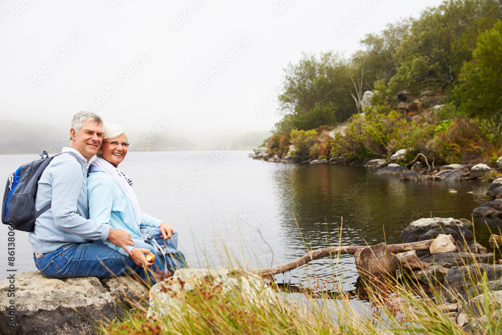 Senior couple sitting together by a lake, looking to camera