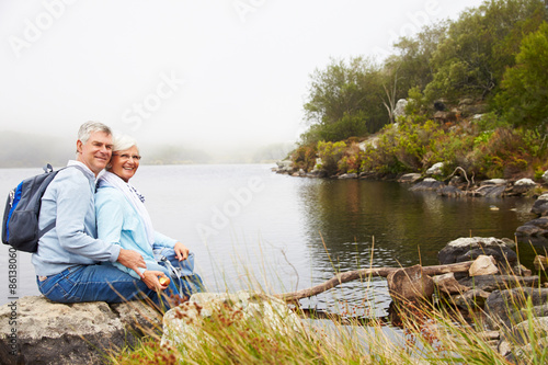 Senior couple sitting together by a lake, looking to camera