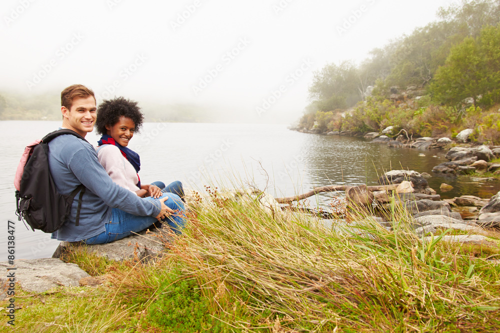 Fototapeta premium Hiking couple relaxing by the edge of a lake, looking to camera