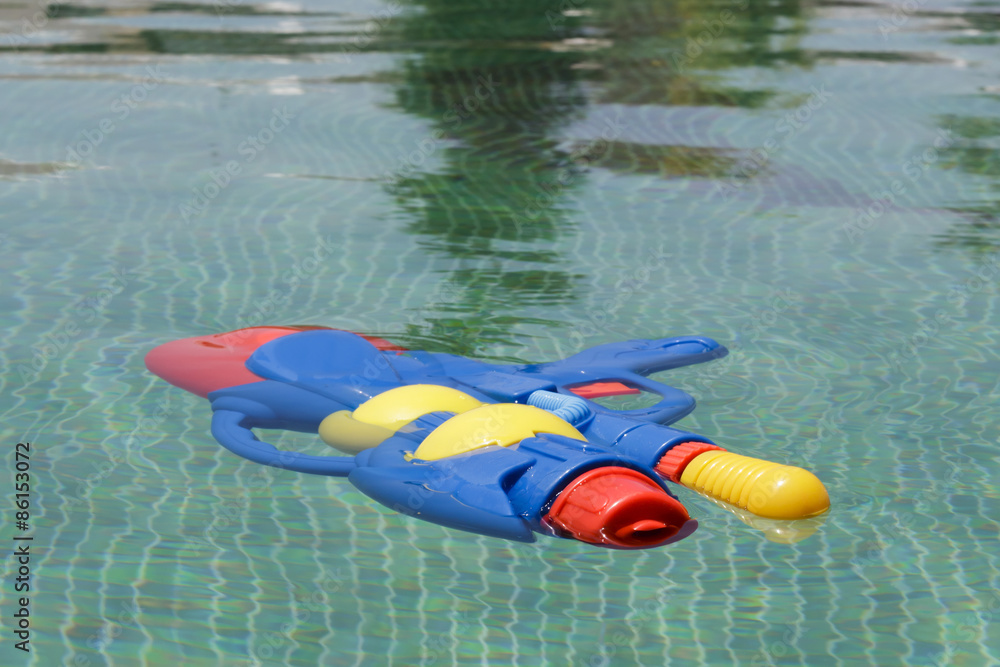 Colorful squirt gun floating in a swimming pool with green tiles floor Colorful squirt gun floating in a swimming pool with green tiles floor
