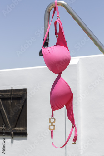 Pink bikini top hanging on a swimming pool shower