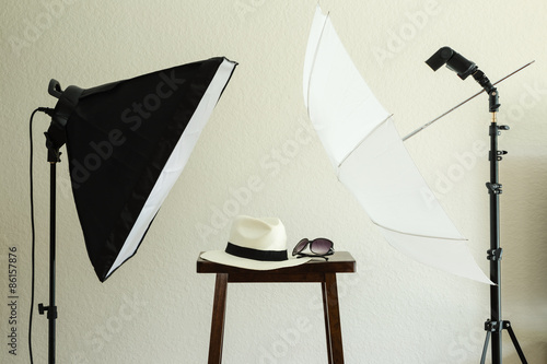 Photo shoot props for a social media profile picture: hat and sunglasses. Includes a softbox, speedlight/strobe, white umbrella. Neutral textured wall background.