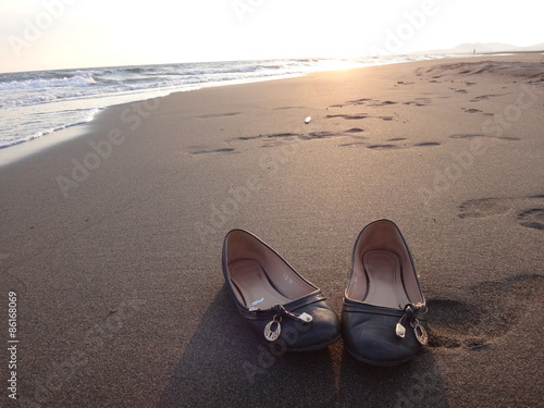 Туфельки, стоящие на песке рядом с набегающими морскими волнами вечером свете закатного солнца