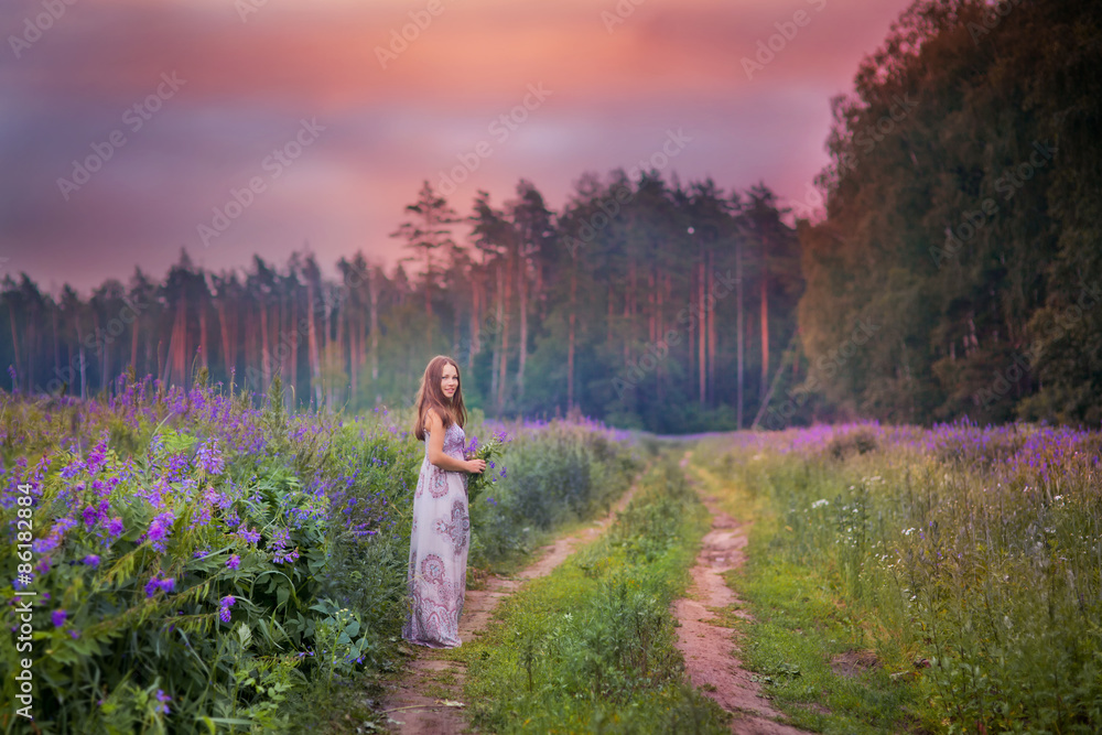 Beautiful young woman standing in the meadow of violet flowers at sunset. Beautiful young woman standing in the meadow of violet flowers at sunset.