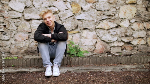 Boy sitting next to the brick wall and smiling to the camera
 photo