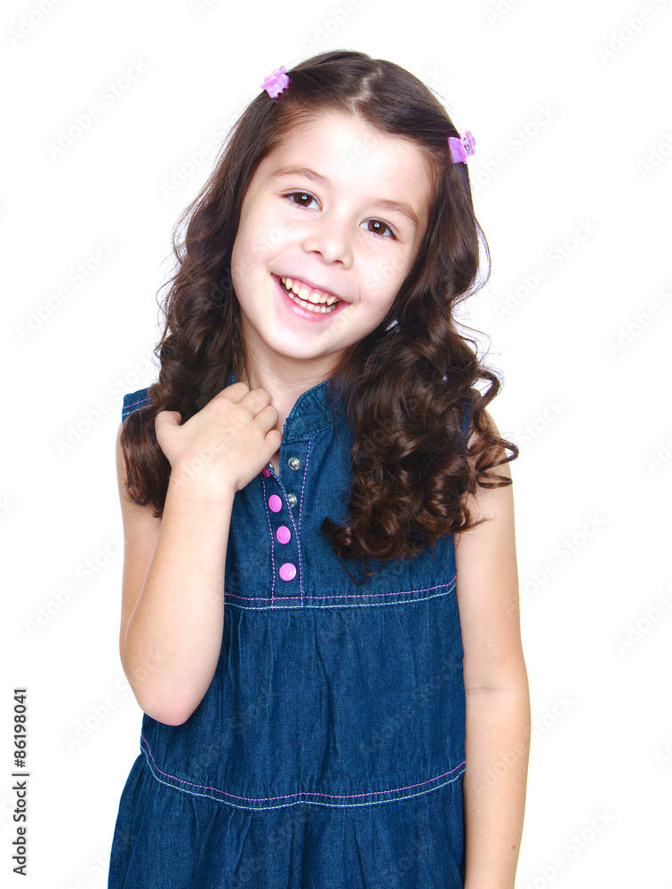 Cute little dark-haired girl in denim dress gently smiling, clos Cute little dark-haired girl in denim dress gently smiling, clos
