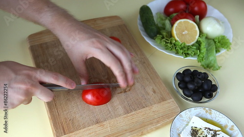 Hand cutting tomato on cutting board with sharp knife photo