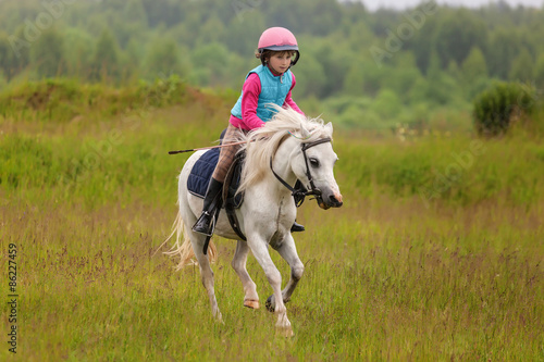 Little girl jumping on the field at a gallop