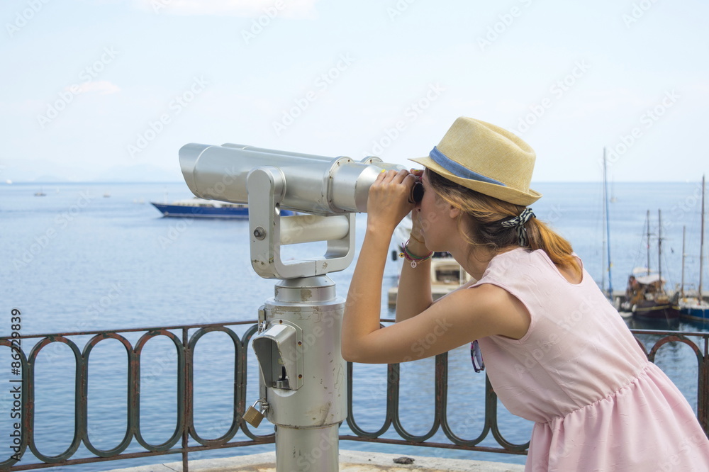 Girl looking thru public binoculars at the seaside wearing straw