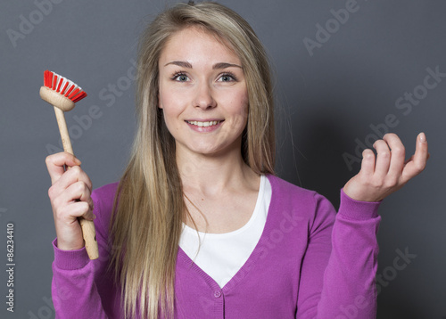 smiling young blond woman wearing purple sweater holding dish brush as magical cleaning tool