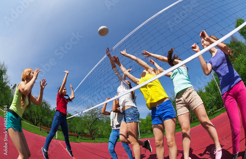 Active teenagers playing volleyball on game court