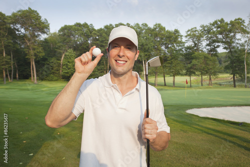 Handsome young golfer holds club and ball on a course