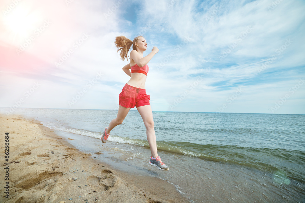 Naklejka premium Young lady running at the sunny summer sand beach. Workout. Jog