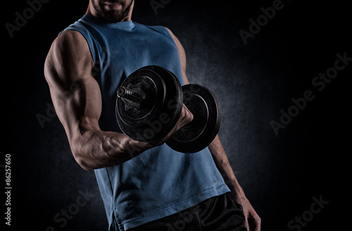 young man with dumbbell flexing muscles over gray background