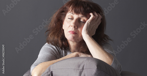 exhausted mature woman resting her face and hands laying down on cushions for comfort while being sick or depressed