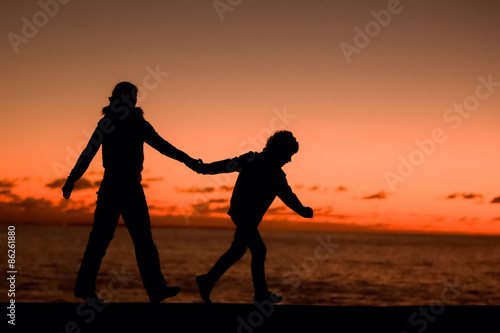 Silhouette of a young mother and her son walking along a pier in