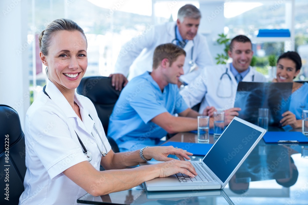 Beautiful smiling doctor typing on keyboard with her team behind Beautiful smiling doctor typing on keyboard with her team behind