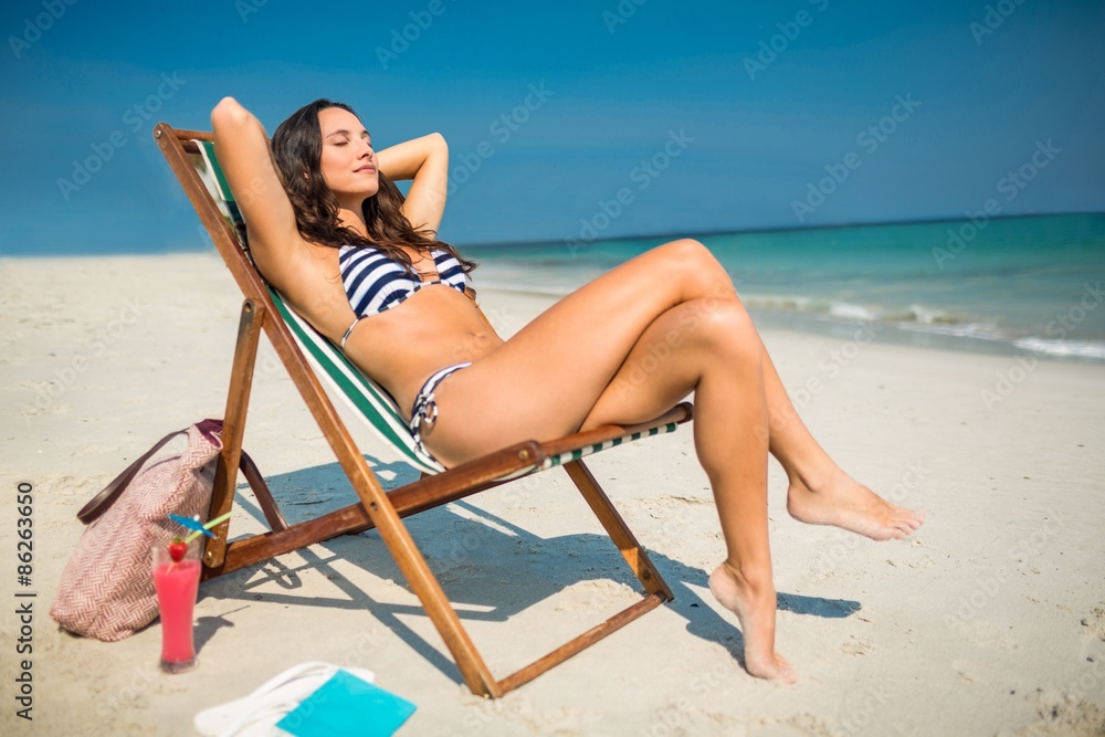 Pretty brunette relaxing on deck chair at the beach