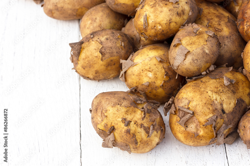 Unwashed new potatoes on white rustic wood. Space for text. Unwashed new potatoes on white rustic wood. Space for text.