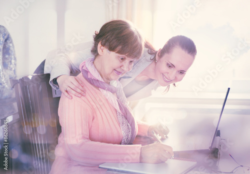 Younger woman helping an elderly person using laptop computer